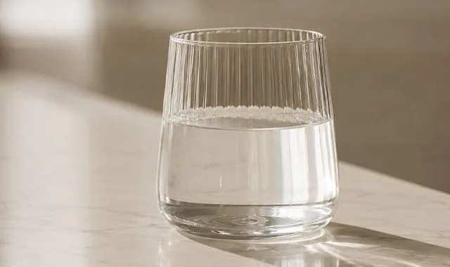 Un bicchiere scanalato di Kangen Water® limpida su un bancone illuminato dal sole
