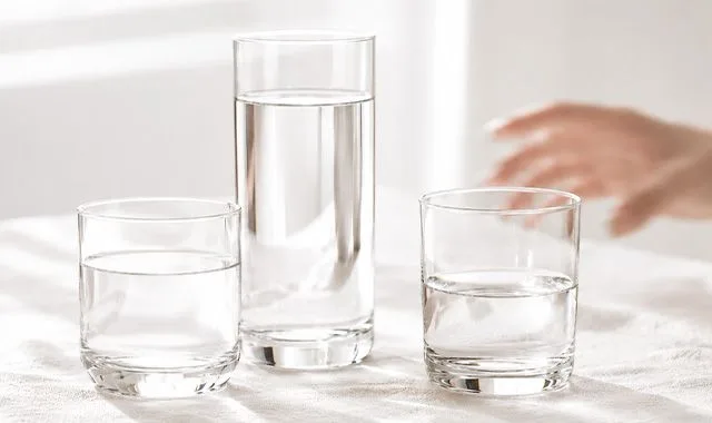Tre bicchieri di acqua fresca in diverse dimensioni su un tavolo luminoso